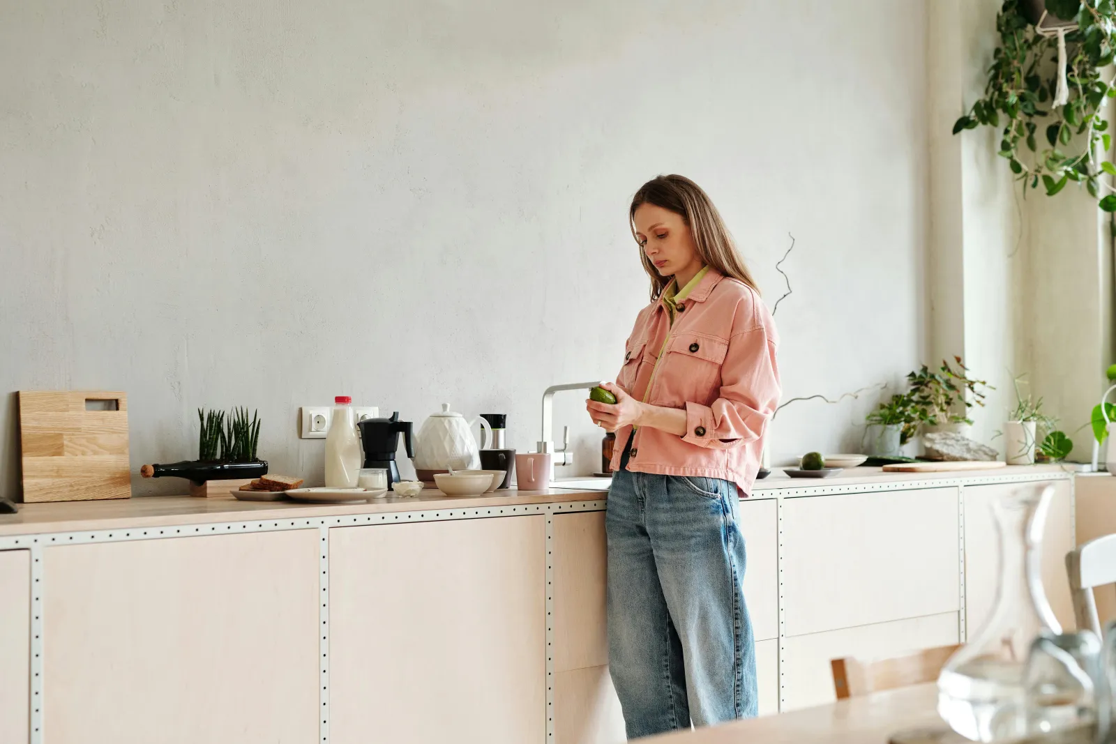 Kvinne står ved kjøkkenbenken i et lyst hjem med planter og mykt dagslys